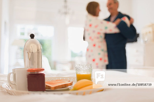 Mature couple in bathrobes dancing behind breakfast in bed