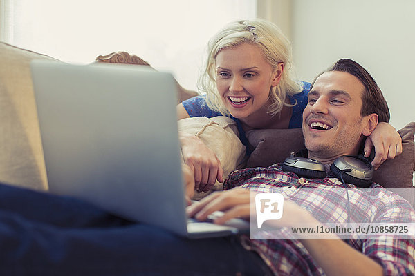 Smiling couple using laptop on living room sofa