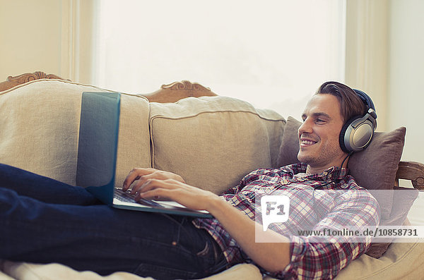Man with headphones using laptop on living room sofa