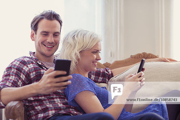 Couple texting with cell phones on living room sofa