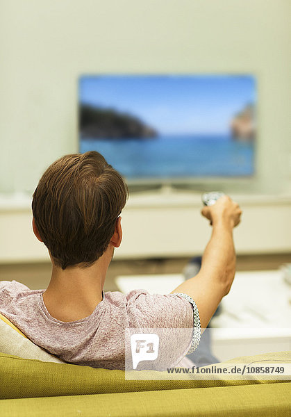 Man watching TV changing channels on living room sofa