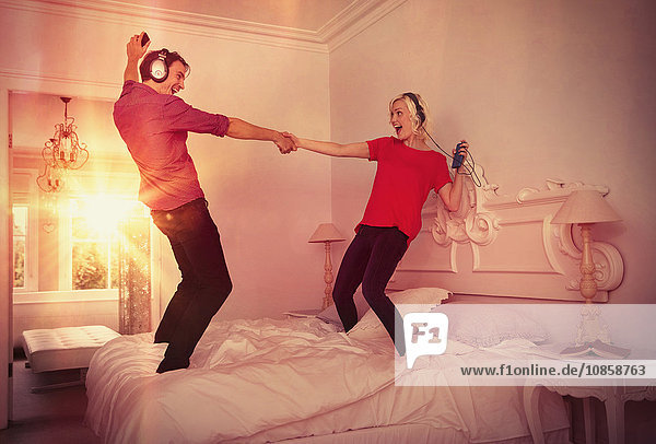 Verspieltes Paar tanzt auf dem Bett und hört Musik mit mp3-Playern und Kopfhörern.