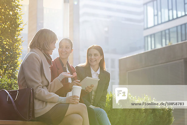 Lächelnde Geschäftsfrauen mit digitalem Tablett beim Kaffee trinken im Freien