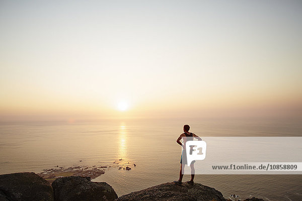 Male runner on rocks looking at sunset ocean view