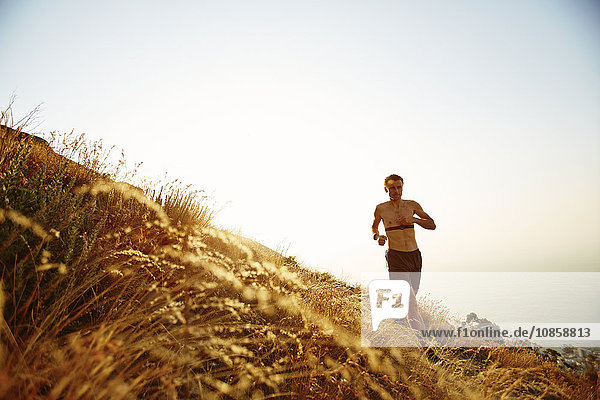 Bare chested man running on sunny hillside