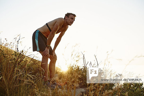Tired male runner with hands on knees on grassy trail