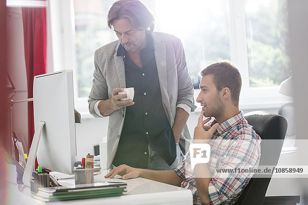 Businessmen drinking coffee and working at computer in office
