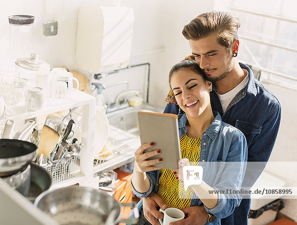 Affectionate young couple using digital tablet in apartment kitchen