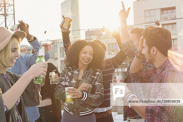 Enthusiastic young adult friends dancing and drinking at rooftop party