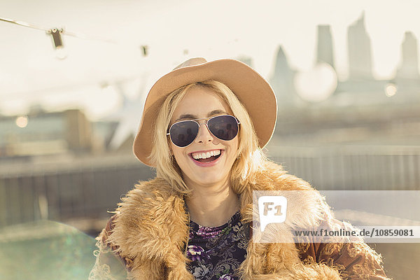 Portrait begeisterte junge Frau mit Hut und Sonnenbrille auf dem sonnigen Dach
