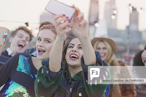Junge Frauen lachen und nehmen Selfie auf der Dachparty mit.