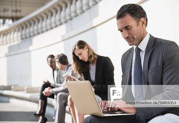 Corporate businessman using laptop on bench outdoors