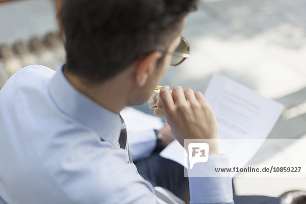 Corporate businessman eating lunch and reading paperwork