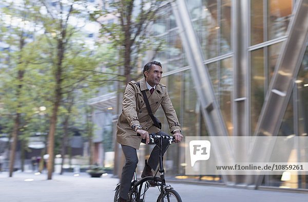 Corporate businessman riding bicycle outside modern building