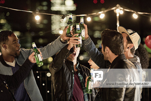 Junge Männer toasten Bierflaschen auf der Dachparty