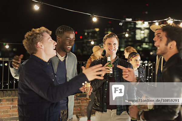 Young men drinking and laughing at rooftop party