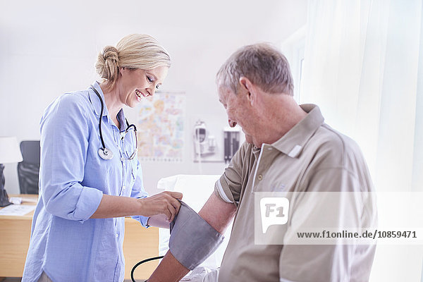 Doctor checking senior man’s blood pressure in examination room