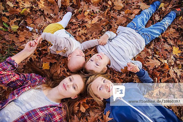 Vier Geschwister auf Herbstblättern liegend