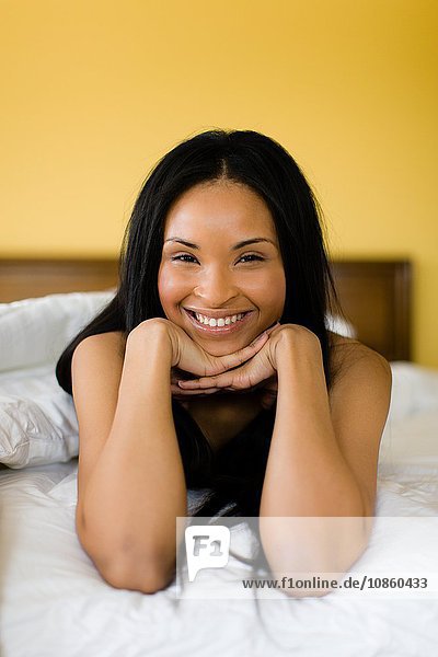 Portrait of happy young woman with long black hair lying on bed