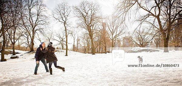 Junges Paar mit Hund spielt im verschneiten Central Park herum  New York  USA