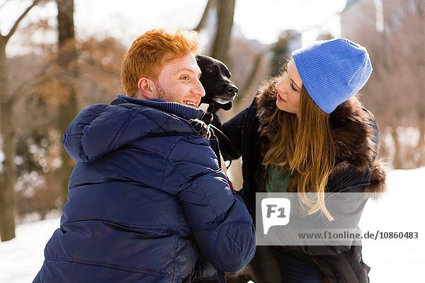 Young couple petting dog in snowy Central Park  New York  USA