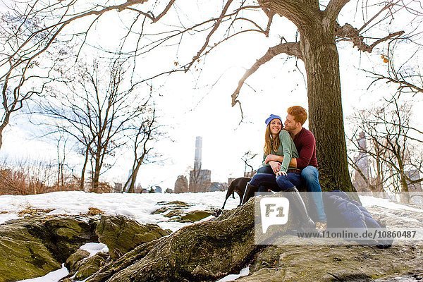 Romantisches junges Paar sitzt mit Hund im verschneiten Central Park  New York  USA