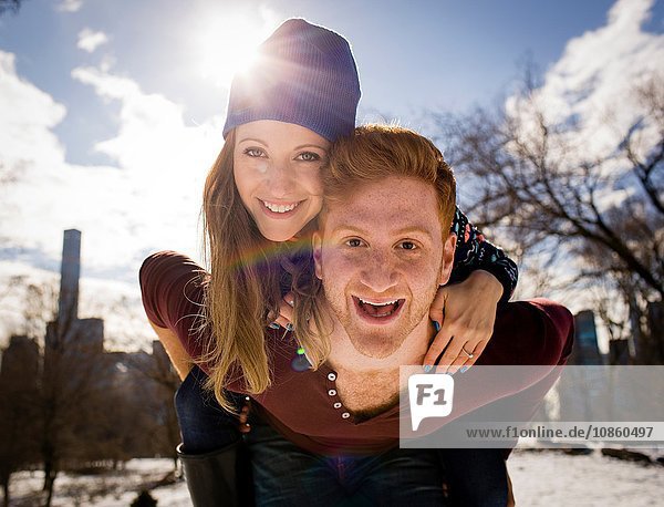 Portrait of young man giving girlfriend a piggy back in snowy Central Park  New York  USA