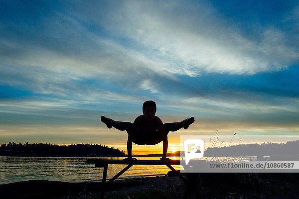 Woman practising yoga by lake at sunset