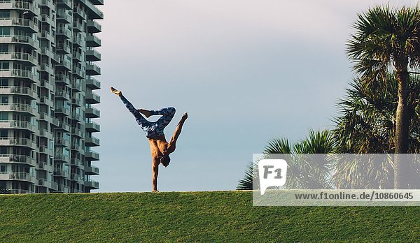 Mature man doing one handed handstand on grass South Pointe Park South Beach Miami Florida USA
