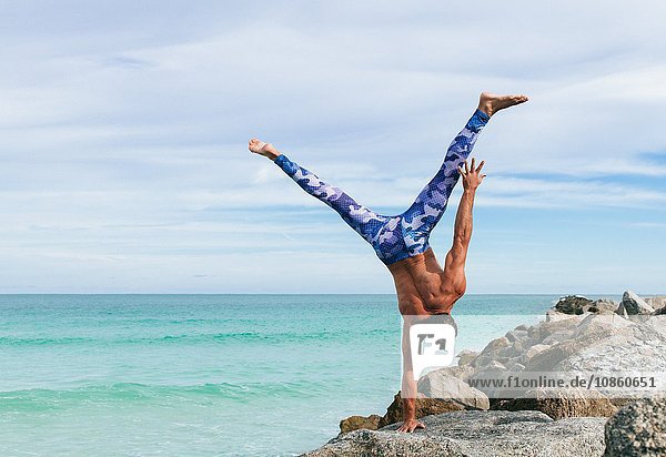 Mature man doing one handed handstand on rock South Pointe Park South Beach Miami Florida USA