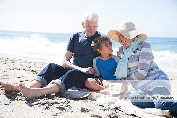 Großeltern und Enkel  am Strand sitzend  lächelnd