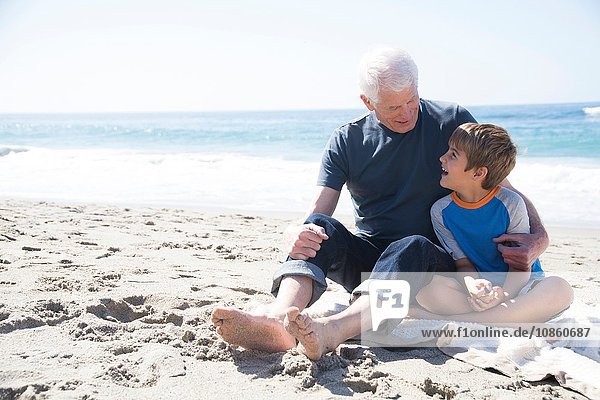 Großvater und Enkel sitzen am Strand und lächeln