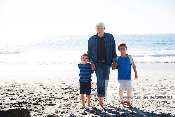 Großvater mit zwei Enkeln  am Strand spazieren  lächelnd