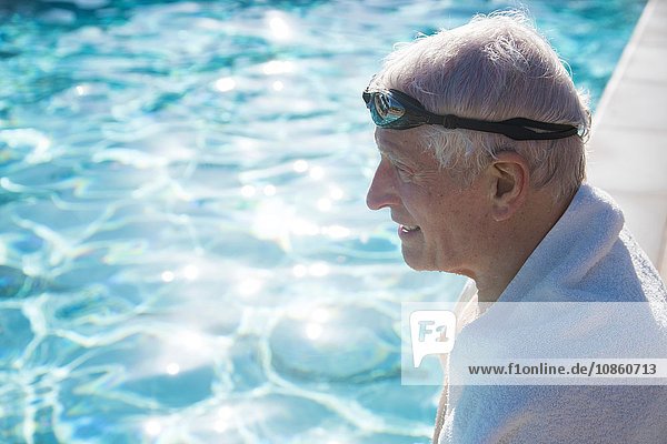 Älterer Mann sitzt am Rand des Freibads  Handtuch um die Schultern