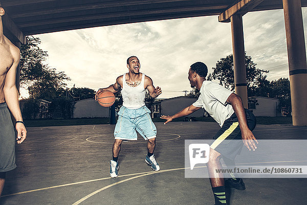 Young men playing basket ball on basket ball court smiling