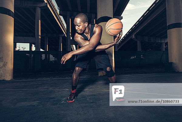 Young man bending forward balancing basketball on hand looking away