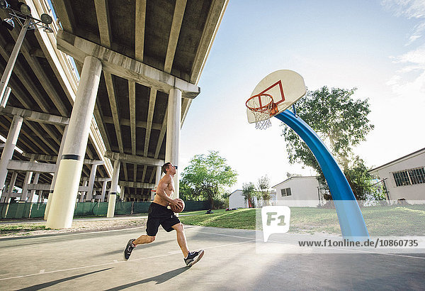 Side view of young man holding basketball running to basketball hoop