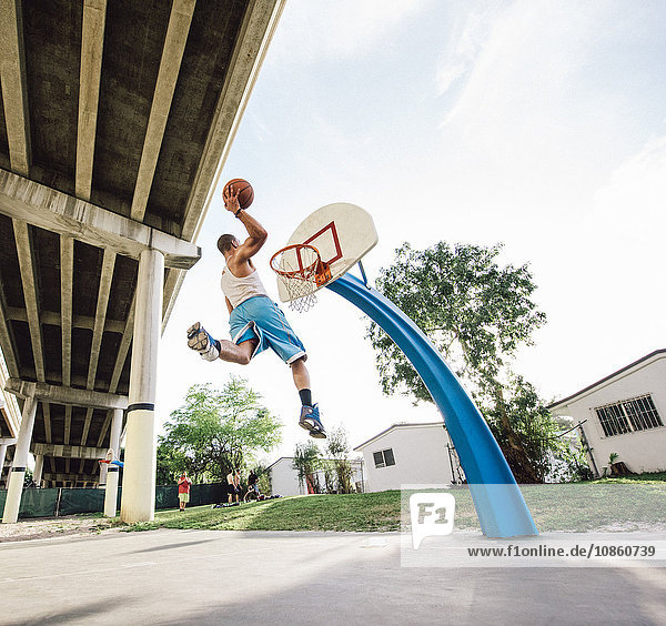 Low angle view of young man in mid air holding basketball jumping for hoop