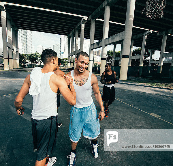 Young men on basketball court connecting with handshake after basketball game smiling