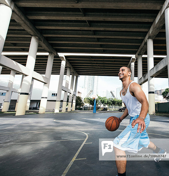 Young man on basketball court holding basketball looking up smiling