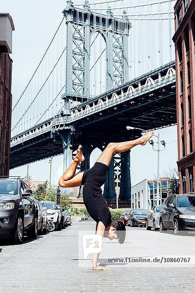 Man practising yoga handstand in front of Manhattan Bridge  New York  USA
