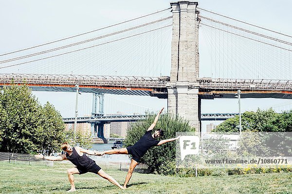 Zwei Männer  die sich im Yoga-Fuss seitwärts lehnen  halten Position vor der Brooklyn Bridge  New York  USA