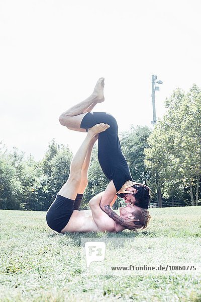 Zwei Männer stehen sich im Park in einer Yogastellung von Angesicht zu Angesicht gegenüber