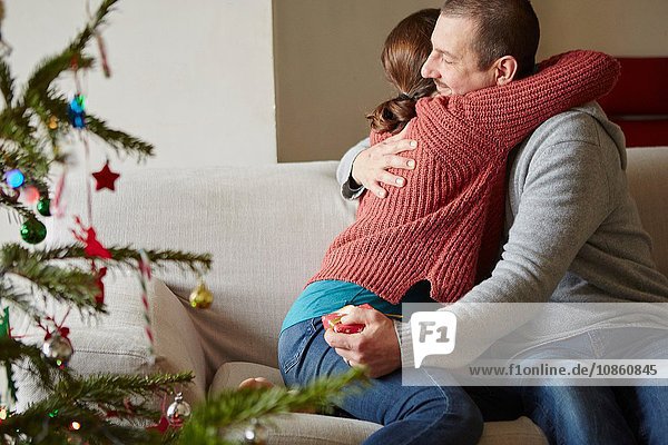 Ehepaar hält Weihnachtsgeschenk und umarmt sich zu Weihnachten auf dem Sofa