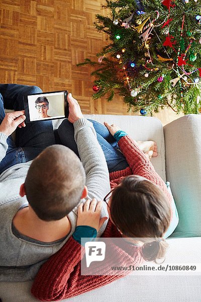 Draufsicht auf das Paar  das zu Weihnachten auf dem Sofa sitzt und einen digitalen Tablet-Videoanruf macht