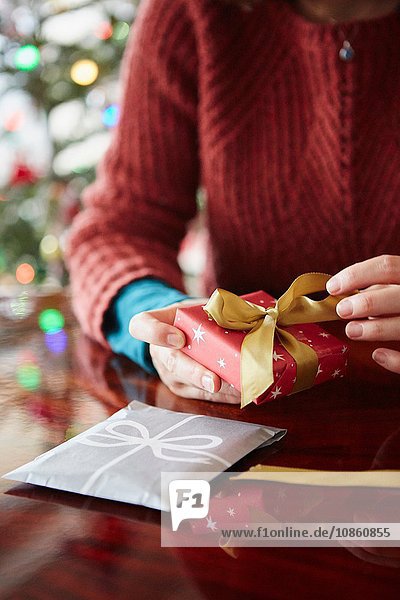 Nahaufnahme von Frauenhänden beim Einpacken des Weihnachtsgeschenks bei Tisch