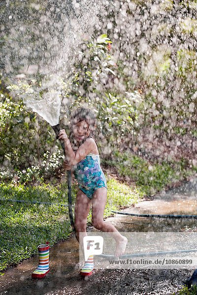 Girl playing with water hose on sidewalk
