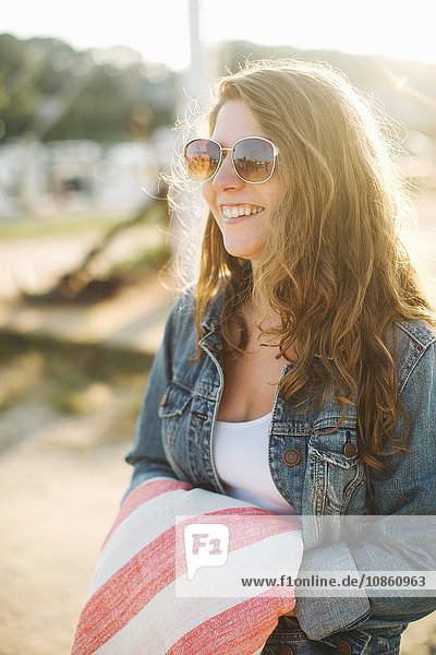 Frauen mit Jeansjacke und Sonnenbrille halten Decke und schauen lächelnd weg
