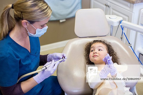 Mädchen auf Zahnarztstuhl beobachtet Zahnarzt bei der Vorbereitung der zahnärztlichen Ausrüstung