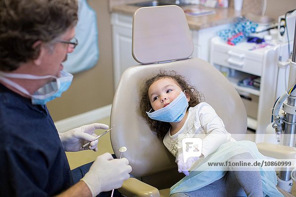 Mädchen auf Zahnarztstuhl schaut dem Zahnarzt bei der Vorbereitung der zahnärztlichen Ausrüstung zu